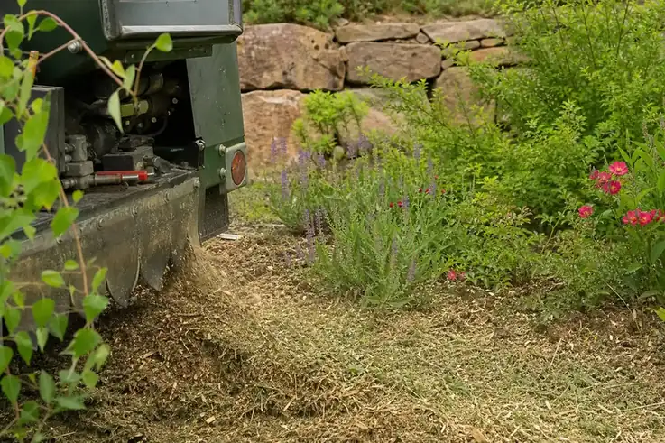 Gros plan sur un broyeur thermique transformant des déchets verts en paillage déposé au pied d'un massif, sur un chantier de débroussaillage près de Rodez.